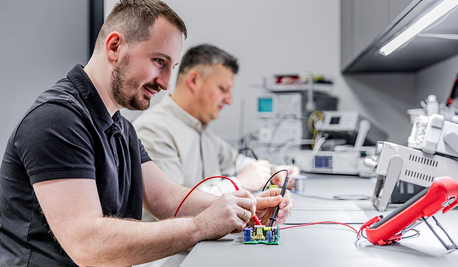 Zwei Techniker in einem Elektroniklabor, die unter geeigneten Lichtverhältnissen präzise Montagearbeiten ausführen
