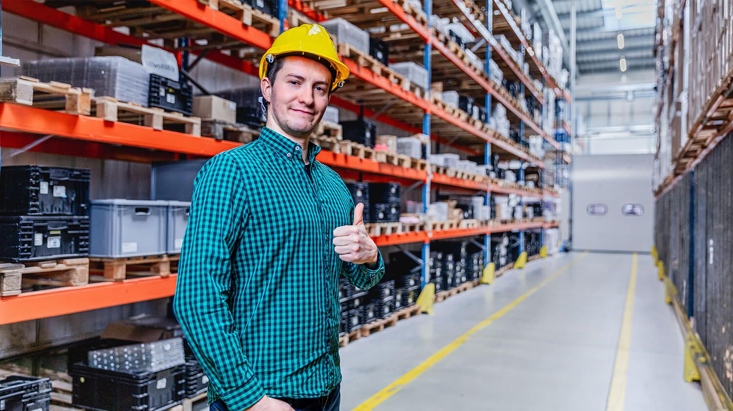 Ein lächelnder Lagerarbeiter mit erhobenem Daumen unterstreicht die Bedeutung einer guten Beleuchtung für den Arbeitskomfort und die Arbeitsleistung.