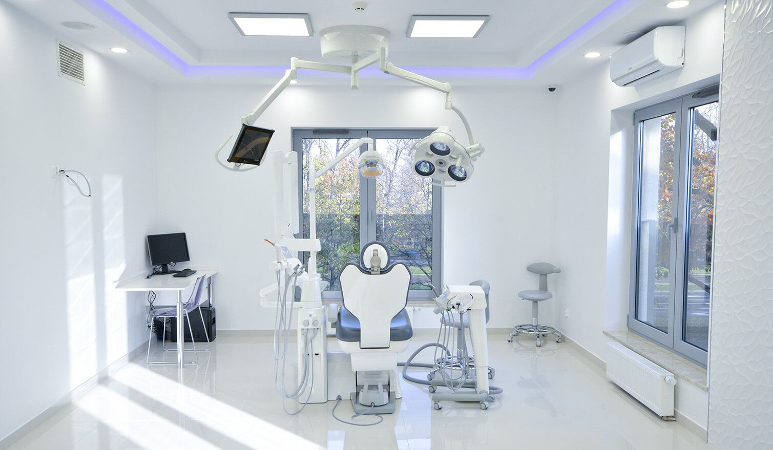 Innenansicht einer Zahnarztpraxis mit Behandlungsstuhl, Computer und Lampe, die die Bedeutung einer angemessenen Beleuchtung in der Zahnmedizin unterstreicht | Lumedic